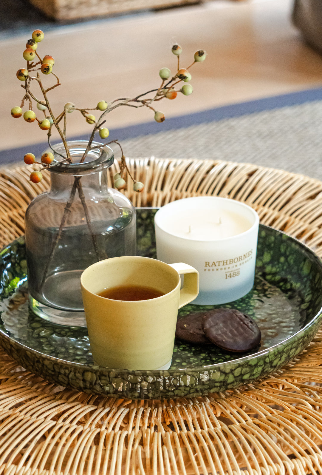Candle on a ceramic plate with a cup of coffee, biscuit and a berry plant in a jar inside a house. 