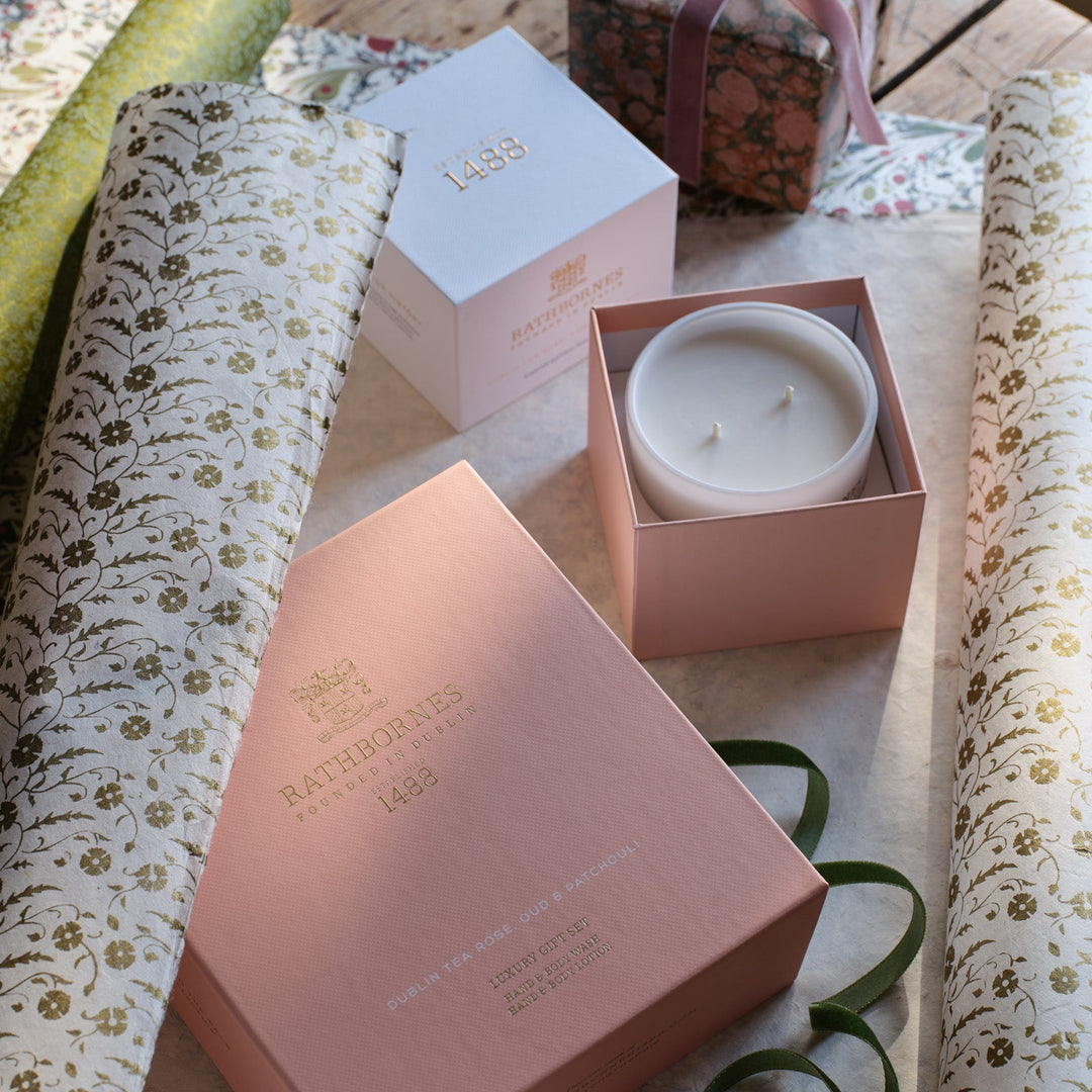Pink gift box with a white candle on a wooden table with floral wrapping paper.