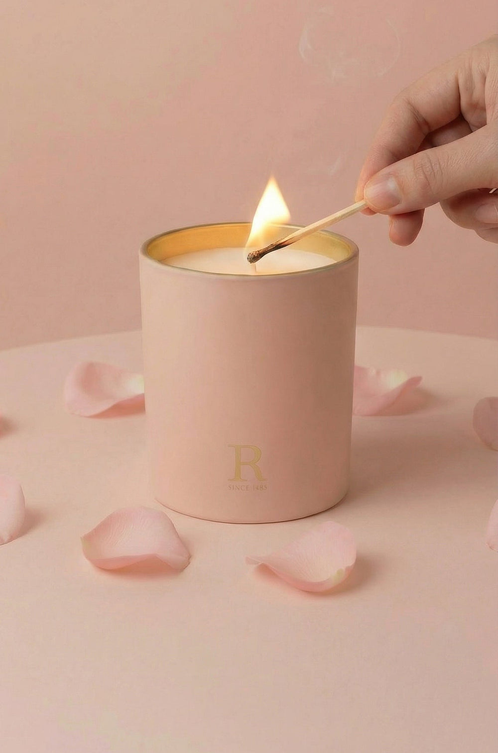 Person lighting a pink candle with a match on a pink background