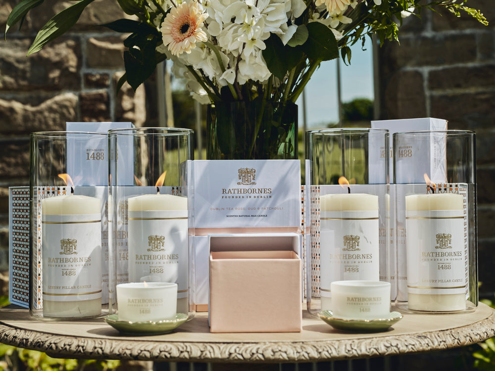Pillars, Scented candles, flowers and packaging place on a wooden table outside on a sunny day.