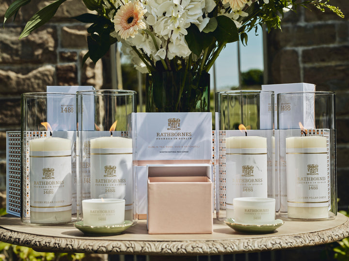 Pillars, Scented candles, flowers and packaging place on a wooden table outside on a sunny day.