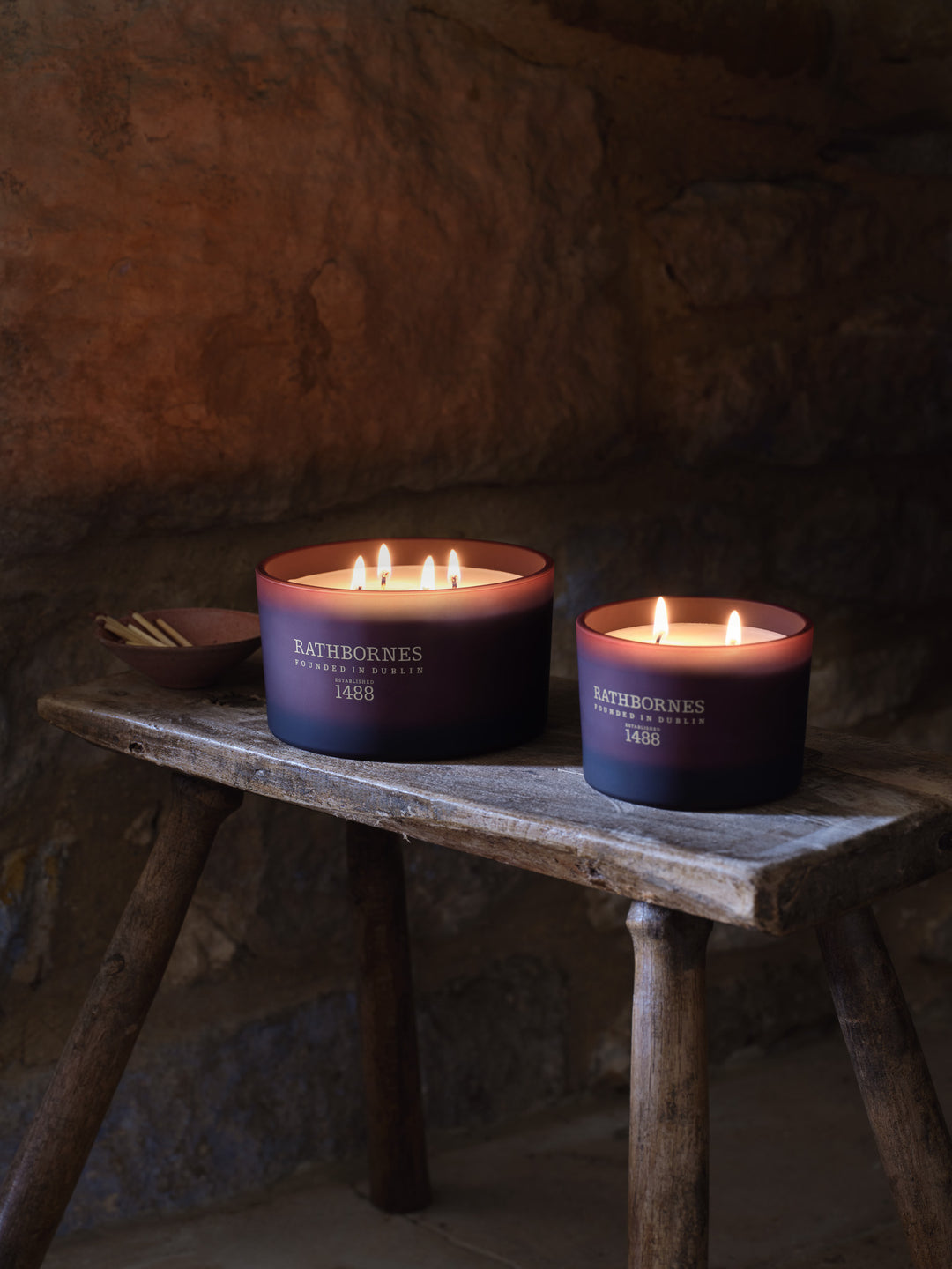 Two lit candles on a rustic wooden table with a dark background