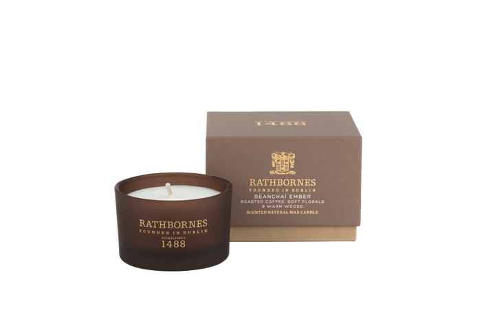Candle in a brown container with 'Rathbornes' branding next to its packaging with transparent background
