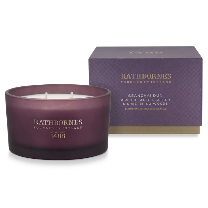Rathbornes Seanchaí Dún scented candle in plum glass beside its aubergine gift box