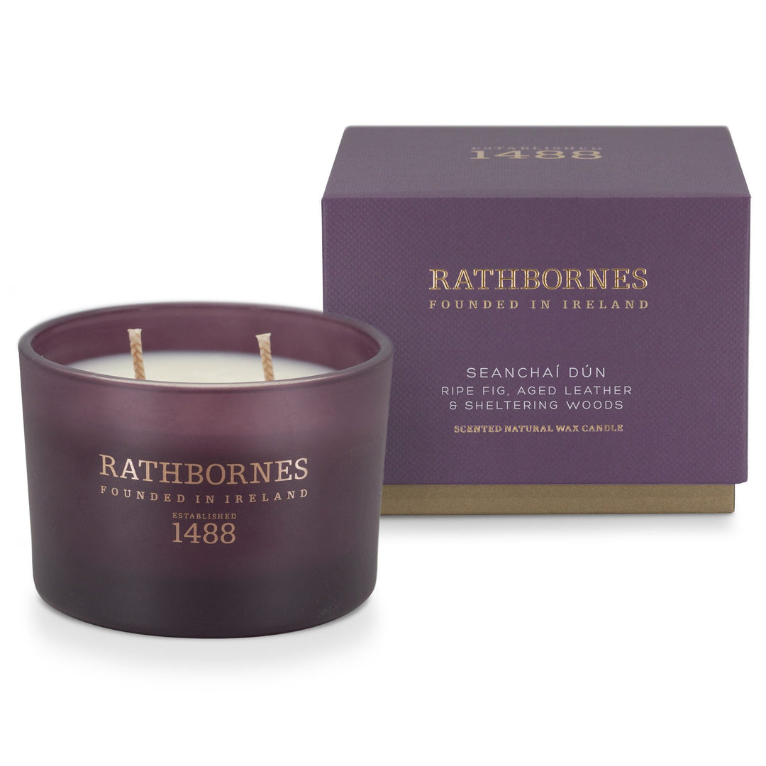Rathbornes Seanchaí Dún (Ripe Fig, Aged Leather & Sheltering Woods) classic 2 wick candle beside its aubergine gift box