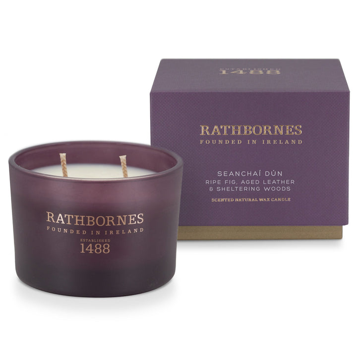 Rathbornes Seanchaí Dún (Ripe Fig, Aged Leather & Sheltering Woods) classic 2 wick candle beside its aubergine gift box