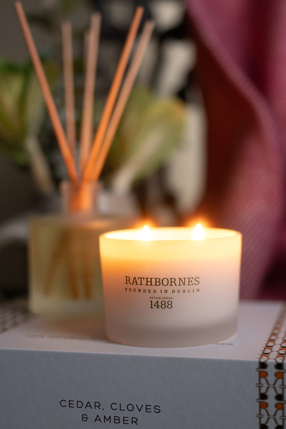 Rathbornes Cedar, Cloves & Amber scented candle lit on its gift box, a luxury gift for her