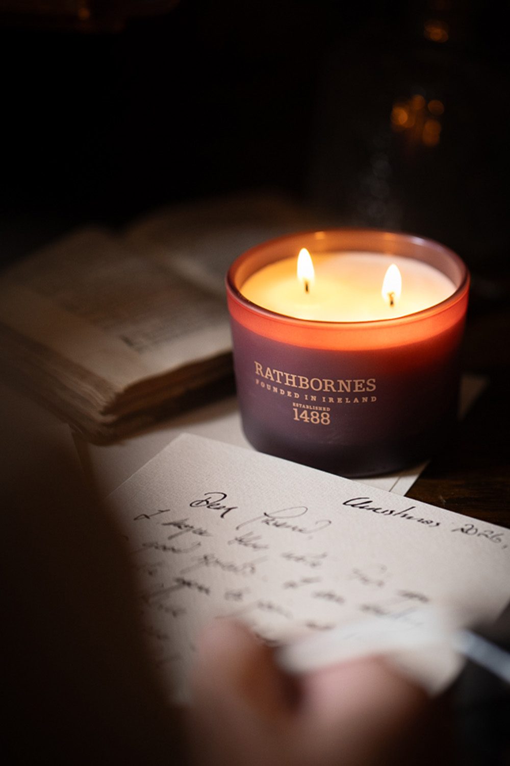 Rathbornes Seanchaí Dún two wick candle lit beside a handwritten Christmas letter and an old book