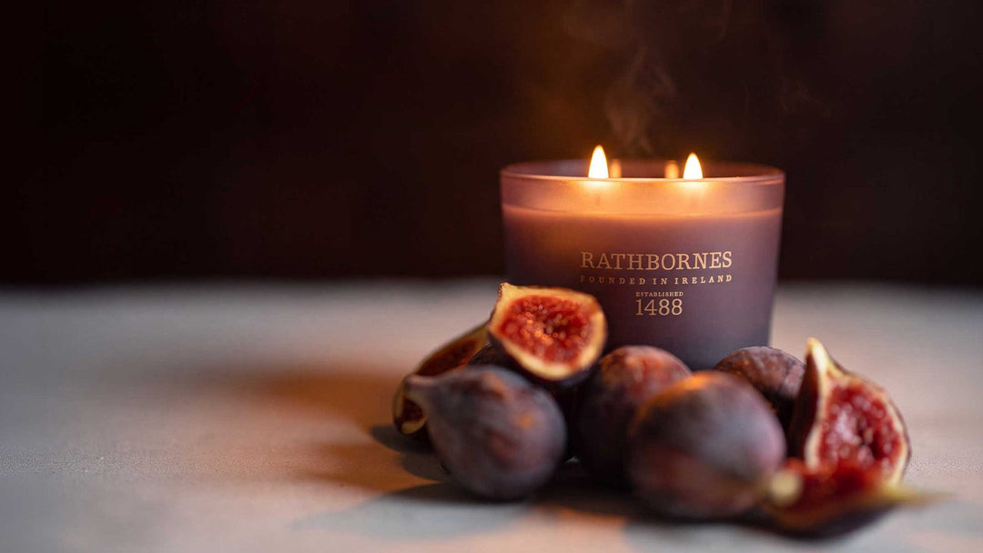 Rathbornes Seanchaí Dún natural wax candle in plum glass, surrounded by fresh figs