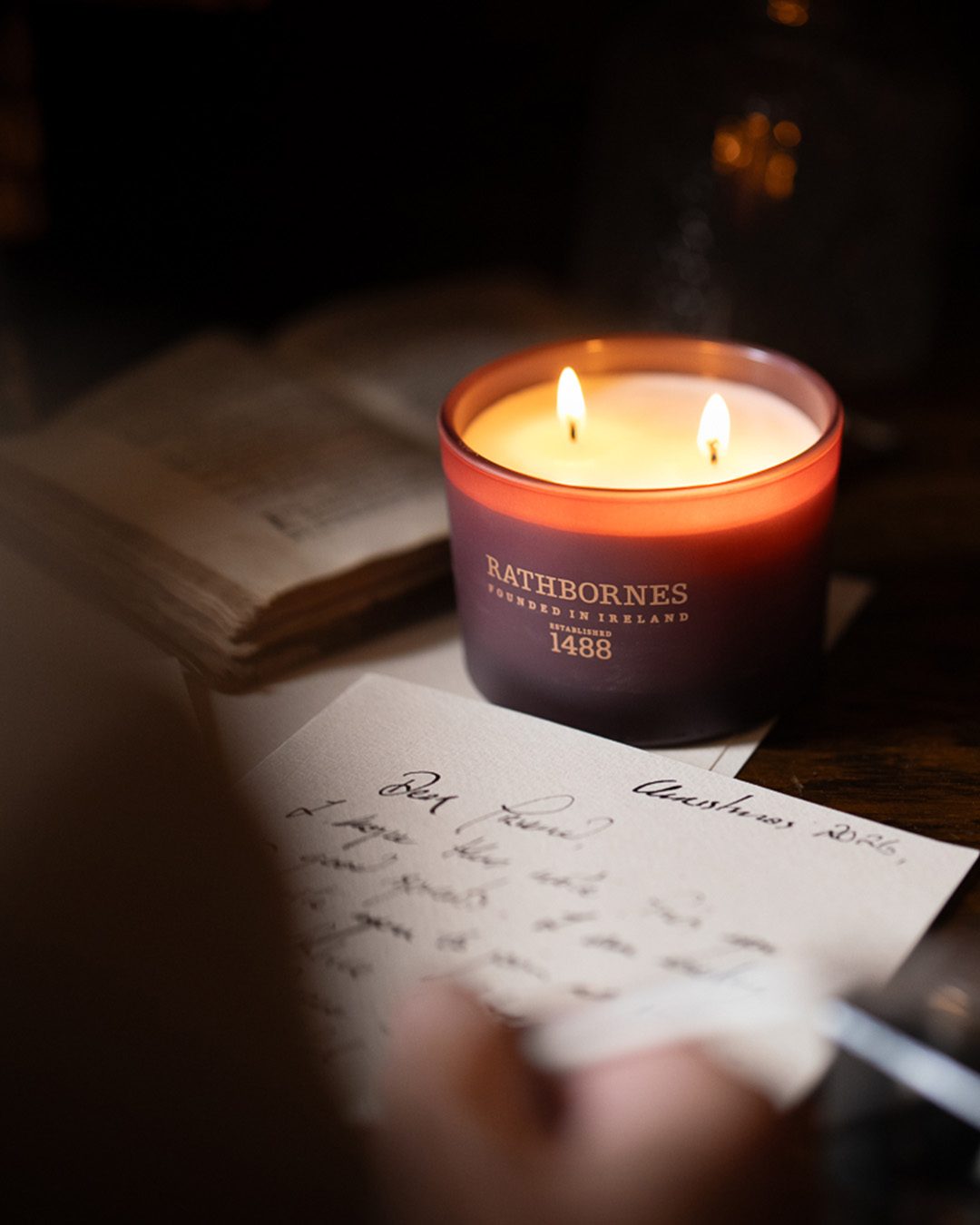 Rathbornes Seanchaí Dún (Ripe Fig, Aged Leather & Sheltering Woods) classic candle glowing on antique desk